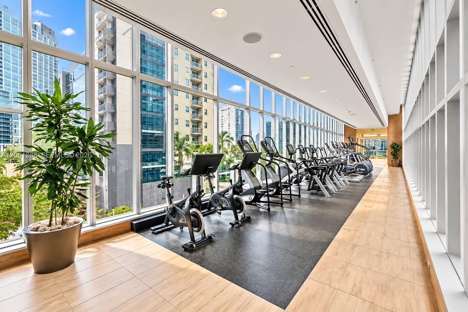 Fitness center featuring floor-to-ceiling windows, wood-finish flooring, integrated recessed lighting, and textured rubberized athletic surfacing