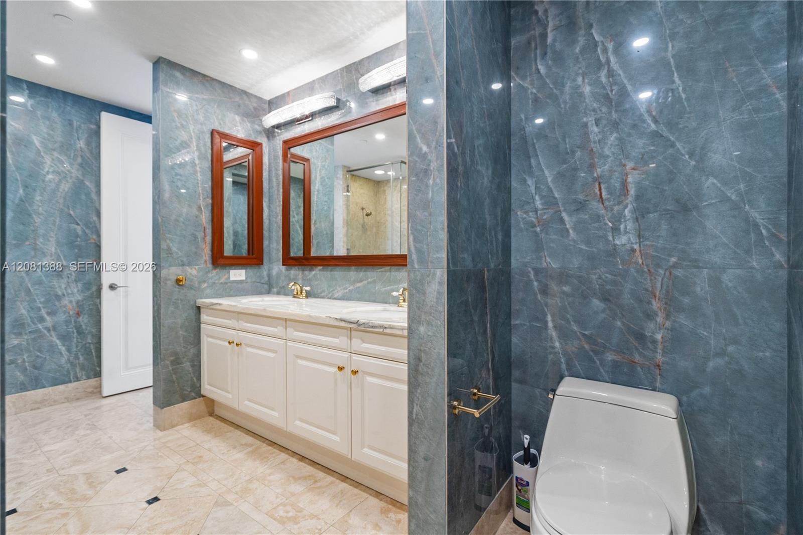 Bathroom featuring floor-to-ceiling blue stone wall tiling, double vanity with white cabinetry, light-toned stone countertop, recessed lighting, and w