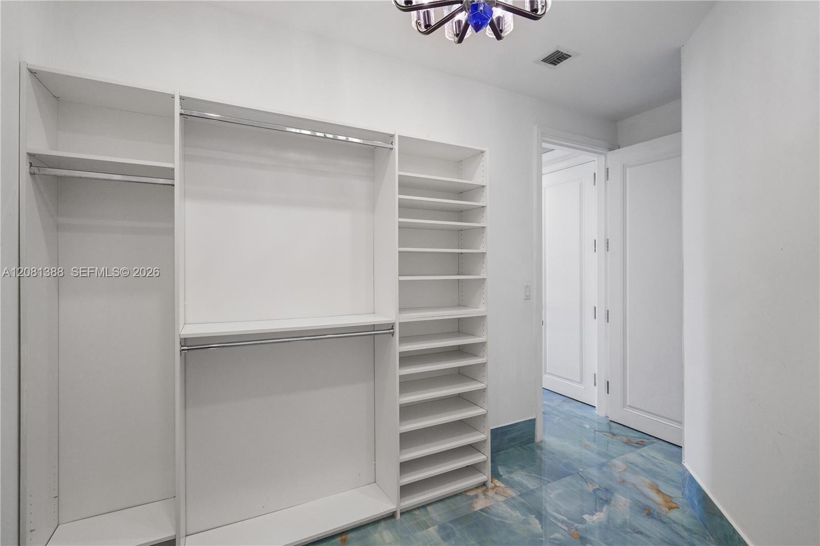 Custom built-in white shelving and cabinetry, multi-level hanging rods, polished blue-toned stone-finish tile flooring, and multi-arm chandelier
