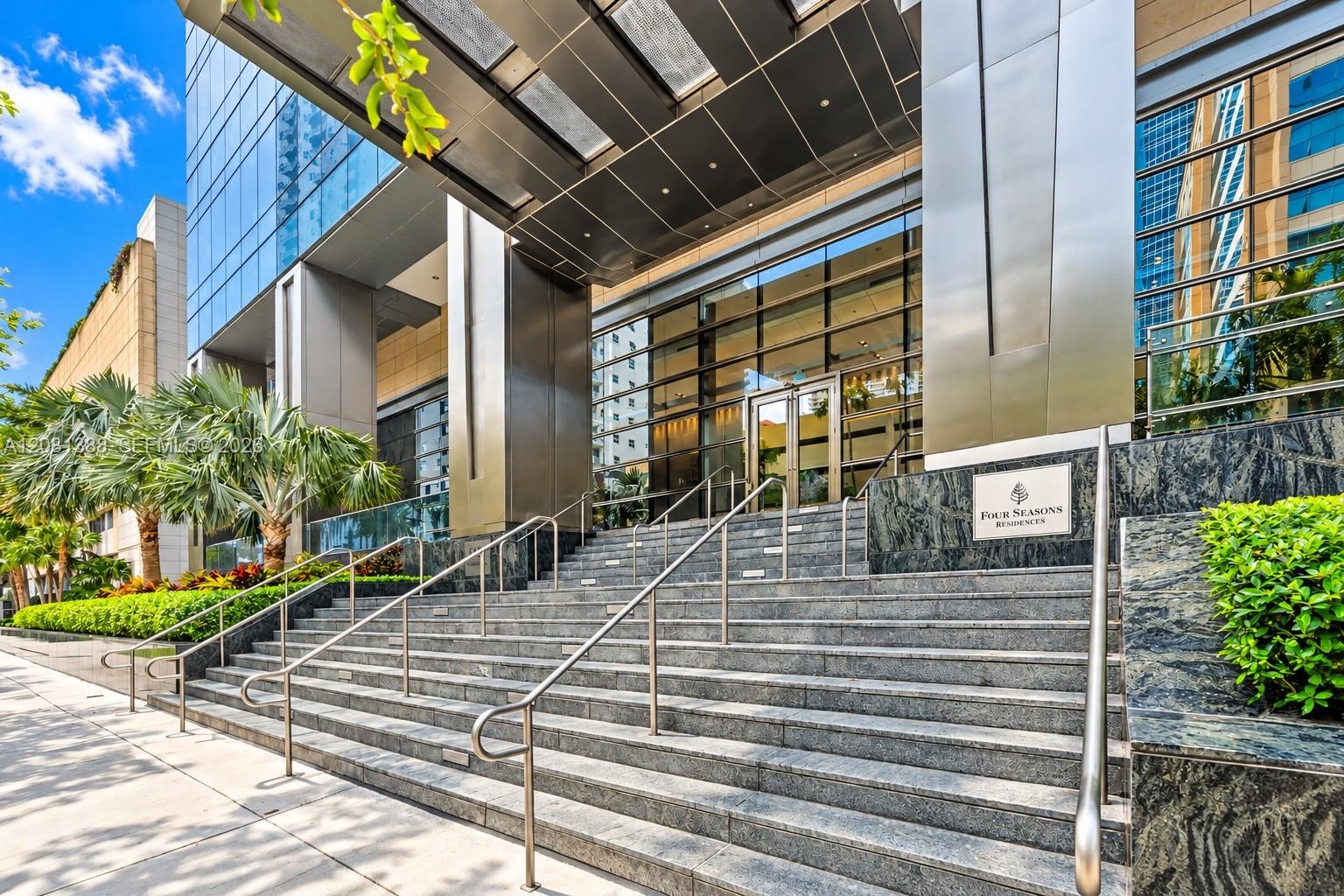 Grand entryway featuring a polished stone staircase, dual metal railings, glass-paneled doors, and a suspended metallic awning