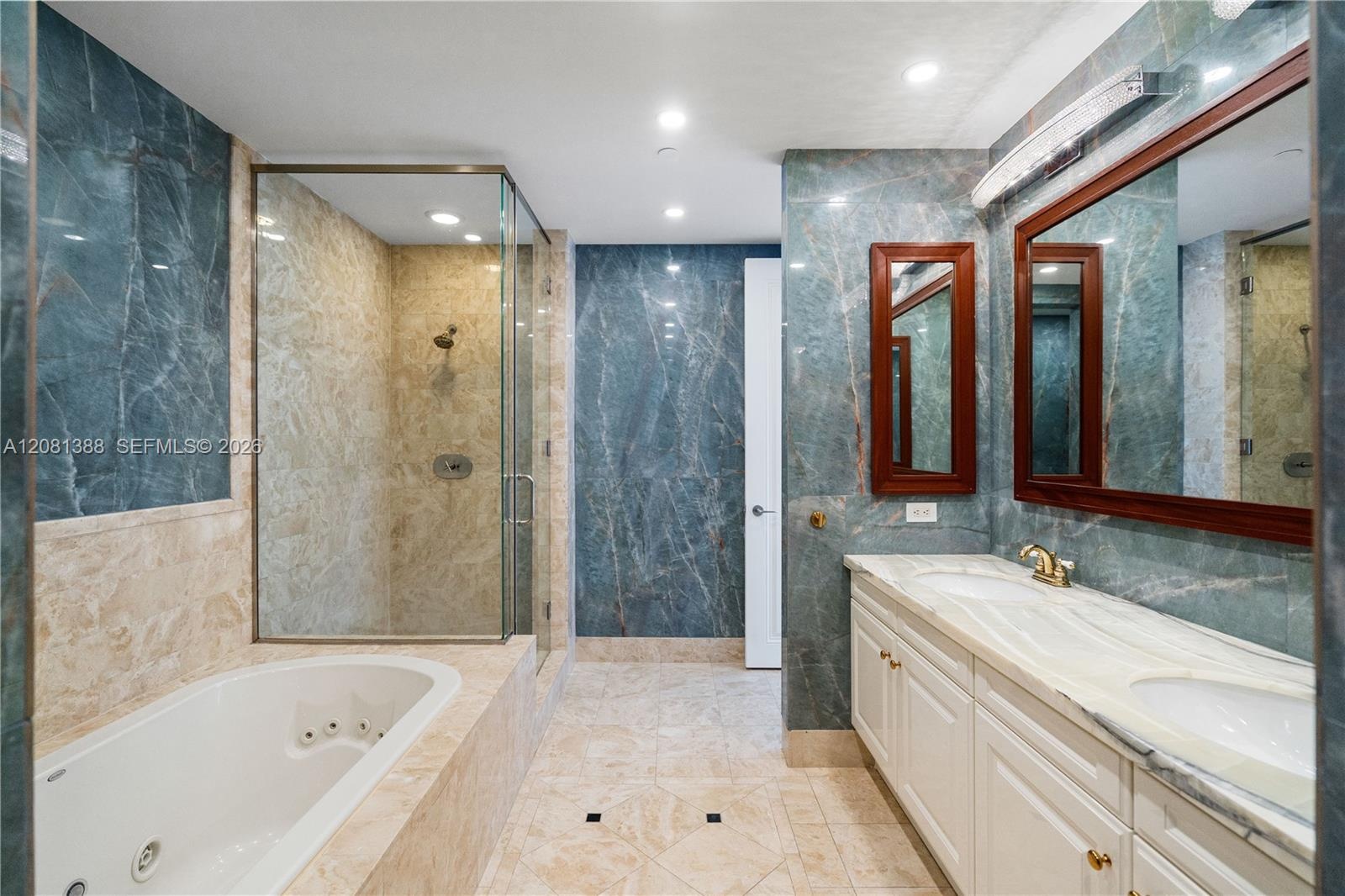 Bathroom featuring blue-veined stone wall cladding, a built-in jetted soaking tub, a walk-in glass-enclosed shower, a double-sink vanity with a stone 