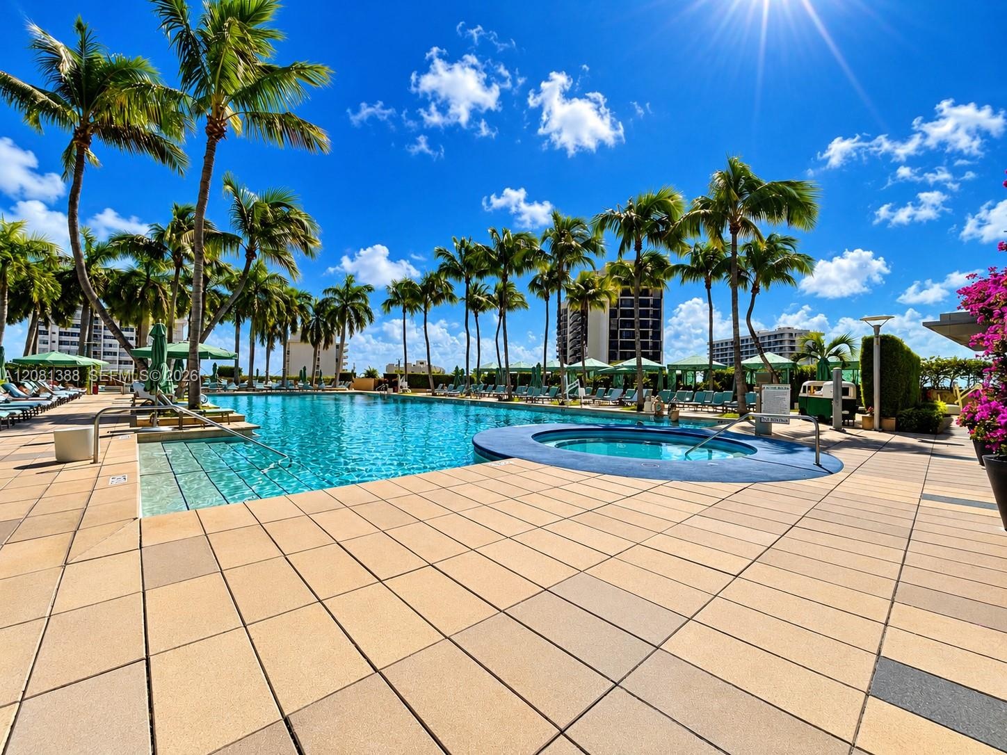 Large swimming pool with integrated circular spa, expansive tiled deck, and mature palm tree landscaping