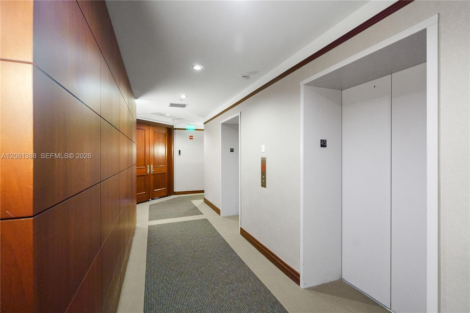 Elevator lobby featuring smooth wood-paneled walls, double-door entryway, and recessed ceiling lighting