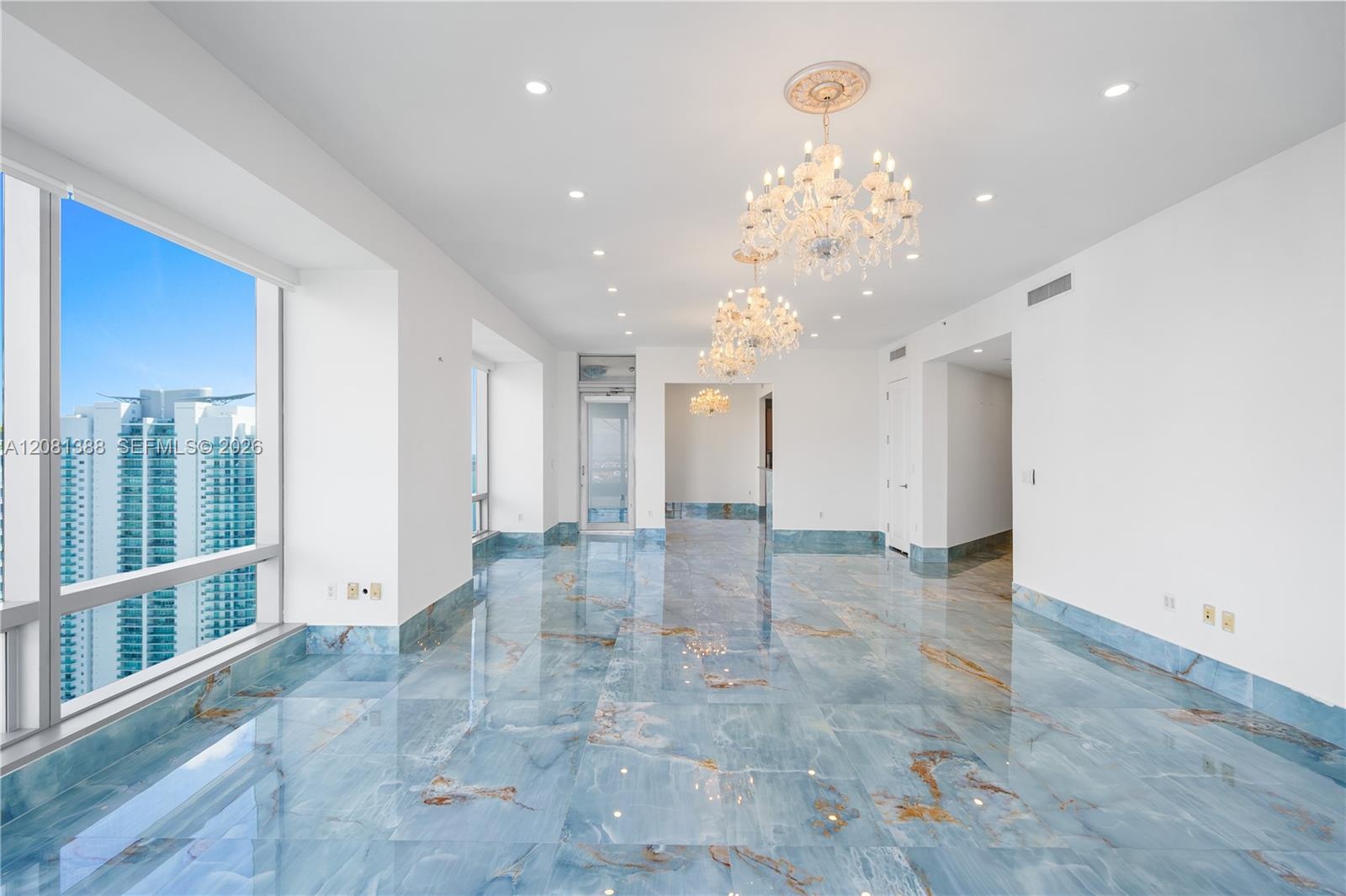 Polished stone flooring with blue and gold veining, floor-to-ceiling windows, crystal chandeliers, recessed lighting, and white wall finishes