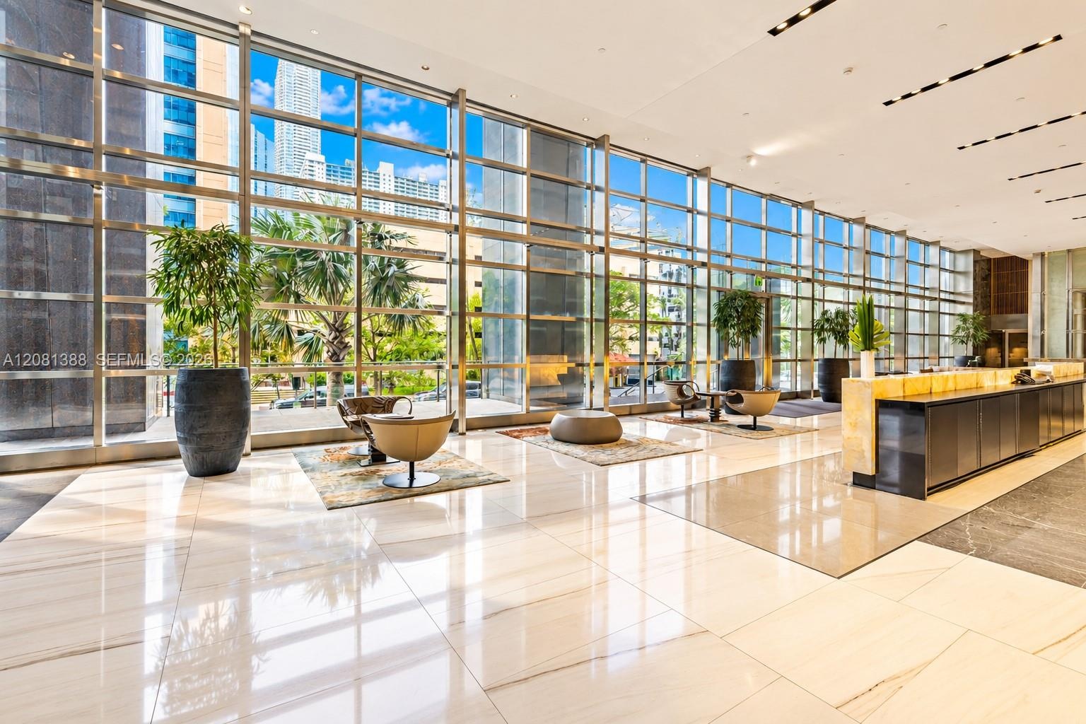 Expansive lobby featuring floor-to-ceiling curtain wall windows, polished stone flooring, recessed lighting, and a built-in reception desk with stone 