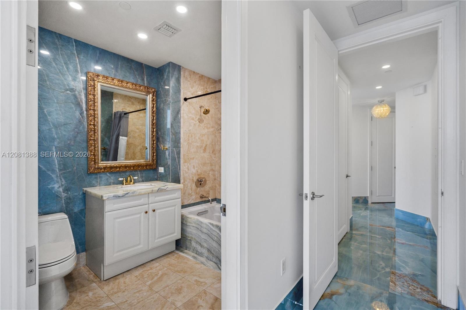 Bathroom featuring blue stone wall cladding, beige stone flooring, a vanity with a light-colored countertop, recessed lighting, and a bathtub with sto