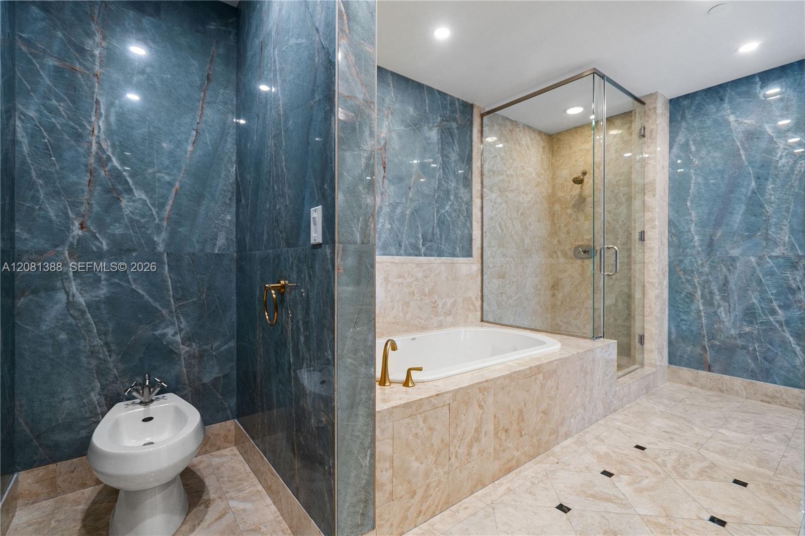 Bathroom featuring floor-to-ceiling blue veined stone wall tiling, a built-in soaking tub with beige stone surround, a glass-enclosed shower with meta