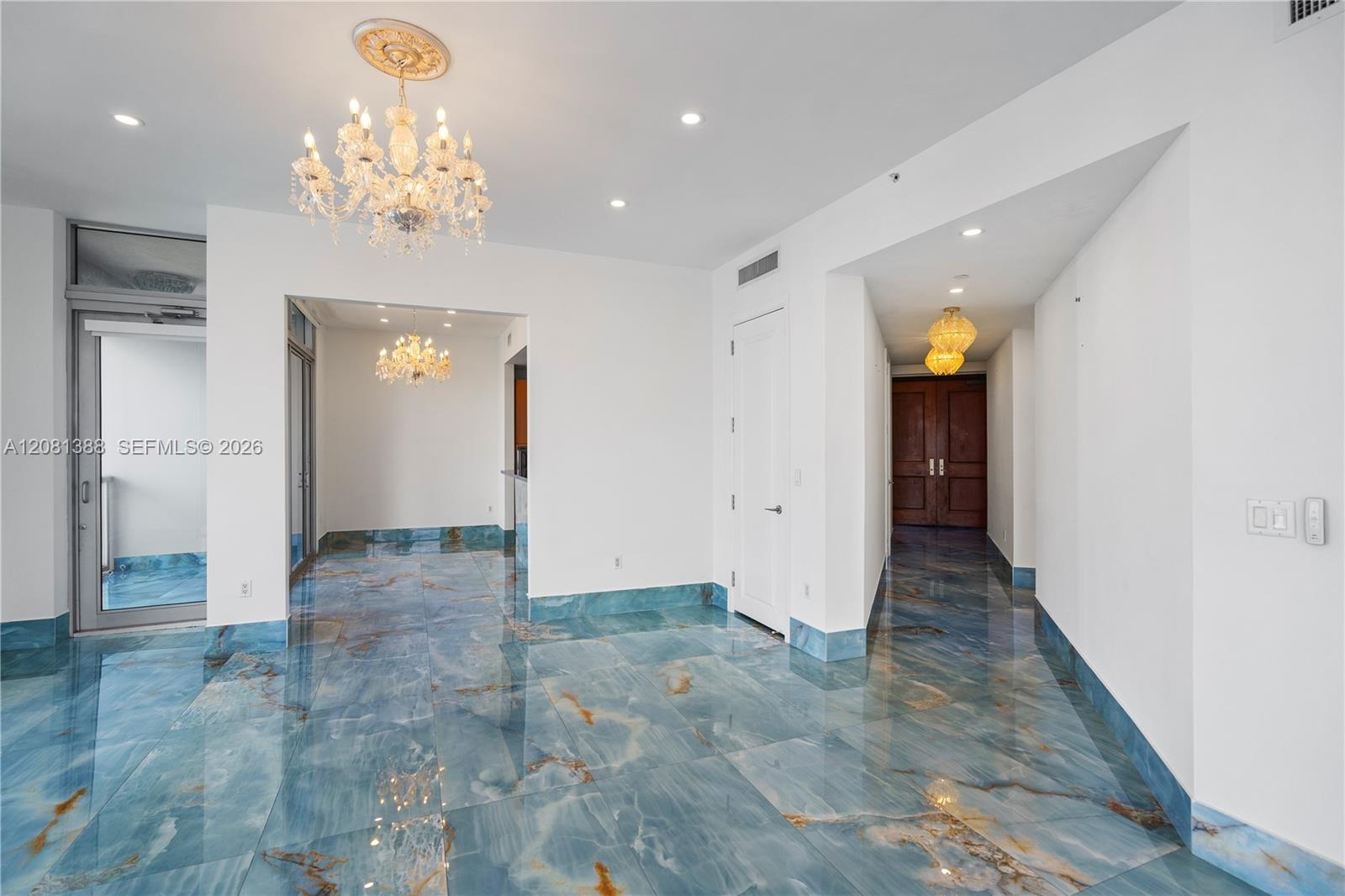 Polished blue stone flooring with gold veining, ornate crystal chandelier, decorative ceiling medallion, recessed lighting, and solid wood double-entr