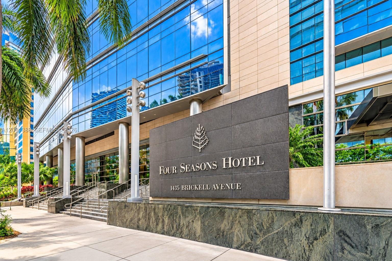 Exterior facade featuring blue-tinted glass curtain walls, stone cladding, metal support columns, and prominent signage at the entry