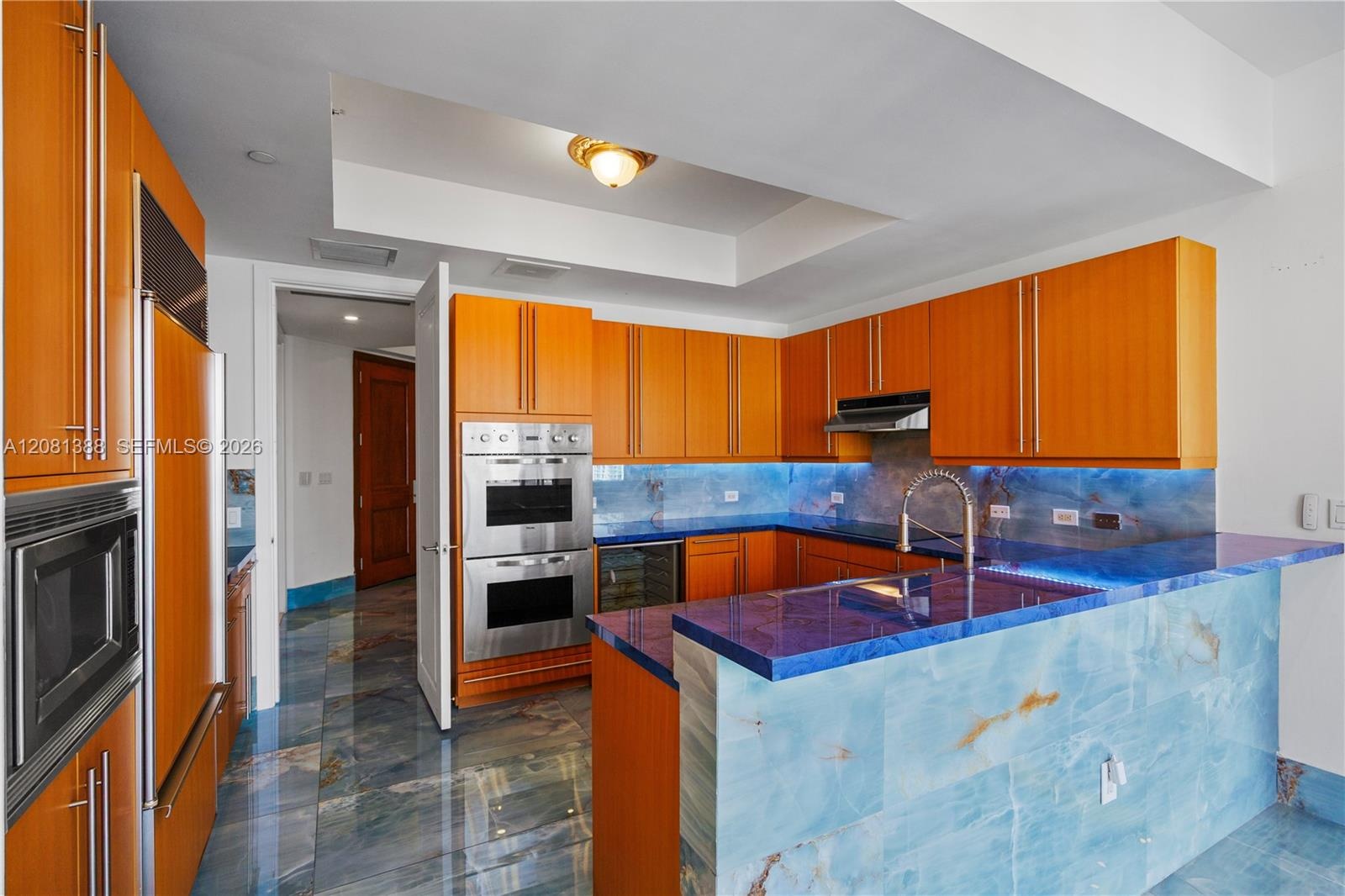 Kitchen featuring natural stone countertops and tile flooring, wood-finish cabinetry, stainless steel double wall ovens, and a recessed ceiling tray
