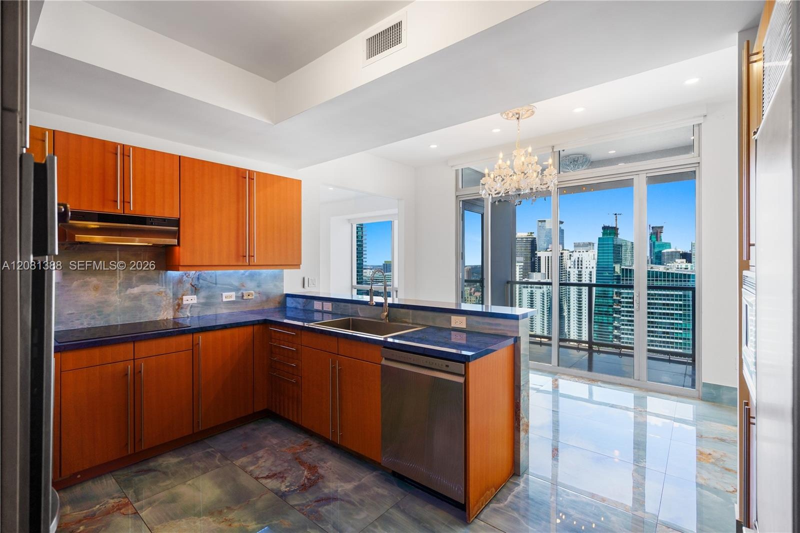 Kitchen featuring wood-finish cabinetry, solid surface countertops, stainless steel appliances, stone flooring, and expansive glass sliding doors