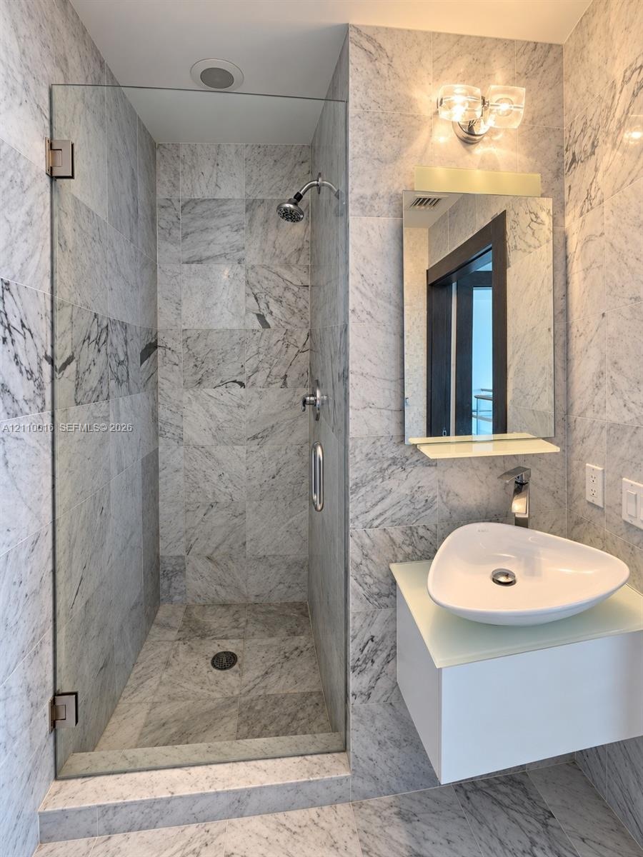 Full-height natural stone tiling, walk-in shower with frameless glass enclosure, wall-mounted floating vanity, vessel sink with chrome faucet, and int