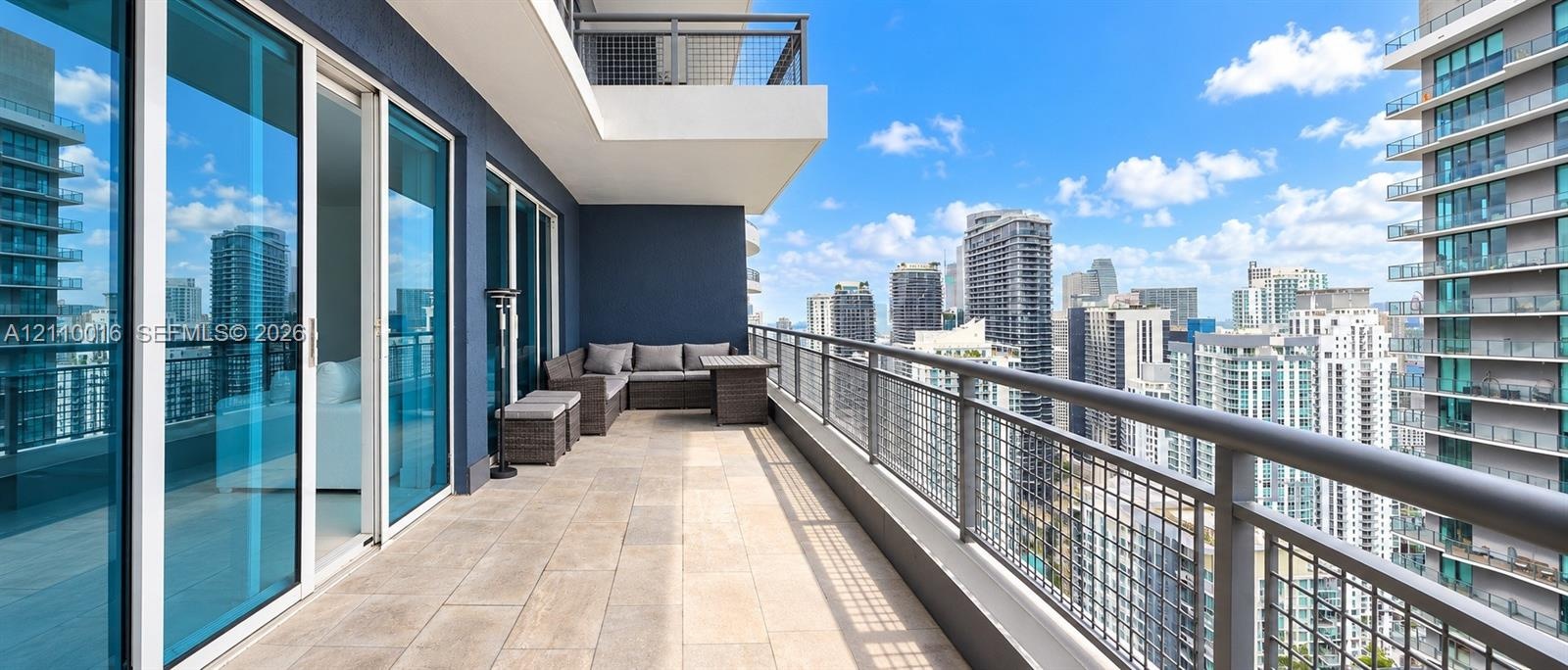 Expansive private balcony featuring floor-to-ceiling glass doors, neutral tile flooring, and a metal mesh railing