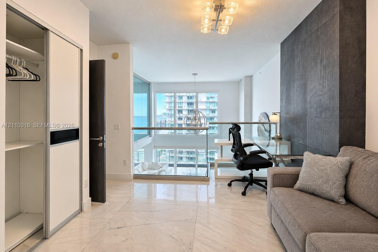 Large-format light-toned stone flooring, floor-to-ceiling dark textured accent wall, glass-panel railing, multi-arm flush-mount ceiling lighting, and 