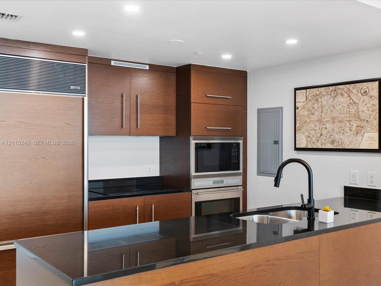 Kitchen featuring wood cabinetry, integrated panel-front refrigerator, dark solid-surface countertops, stainless steel wall oven and microwave, and a 