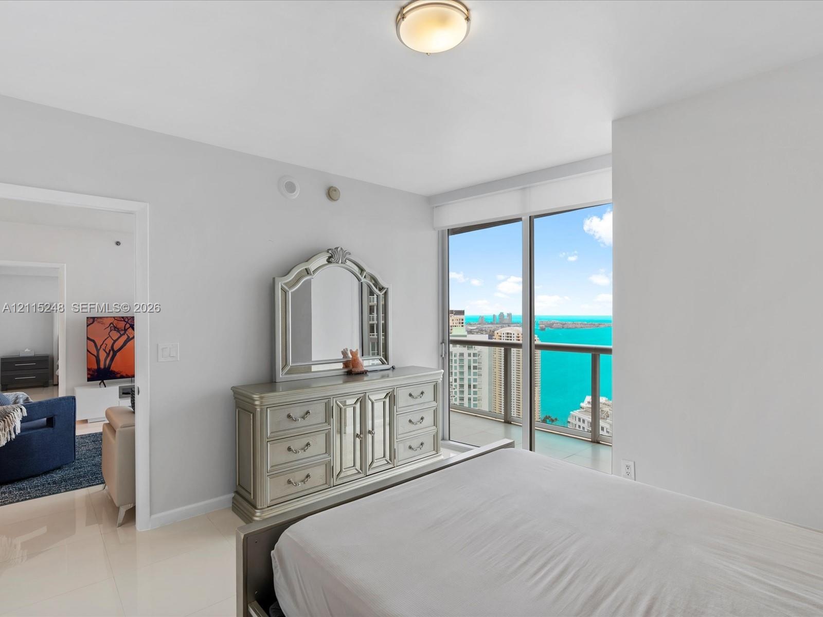 Floor-to-ceiling windows, porcelain tile flooring, neutral wall palette, flush-mount lighting, and private balcony with coastal and cityscape scenery