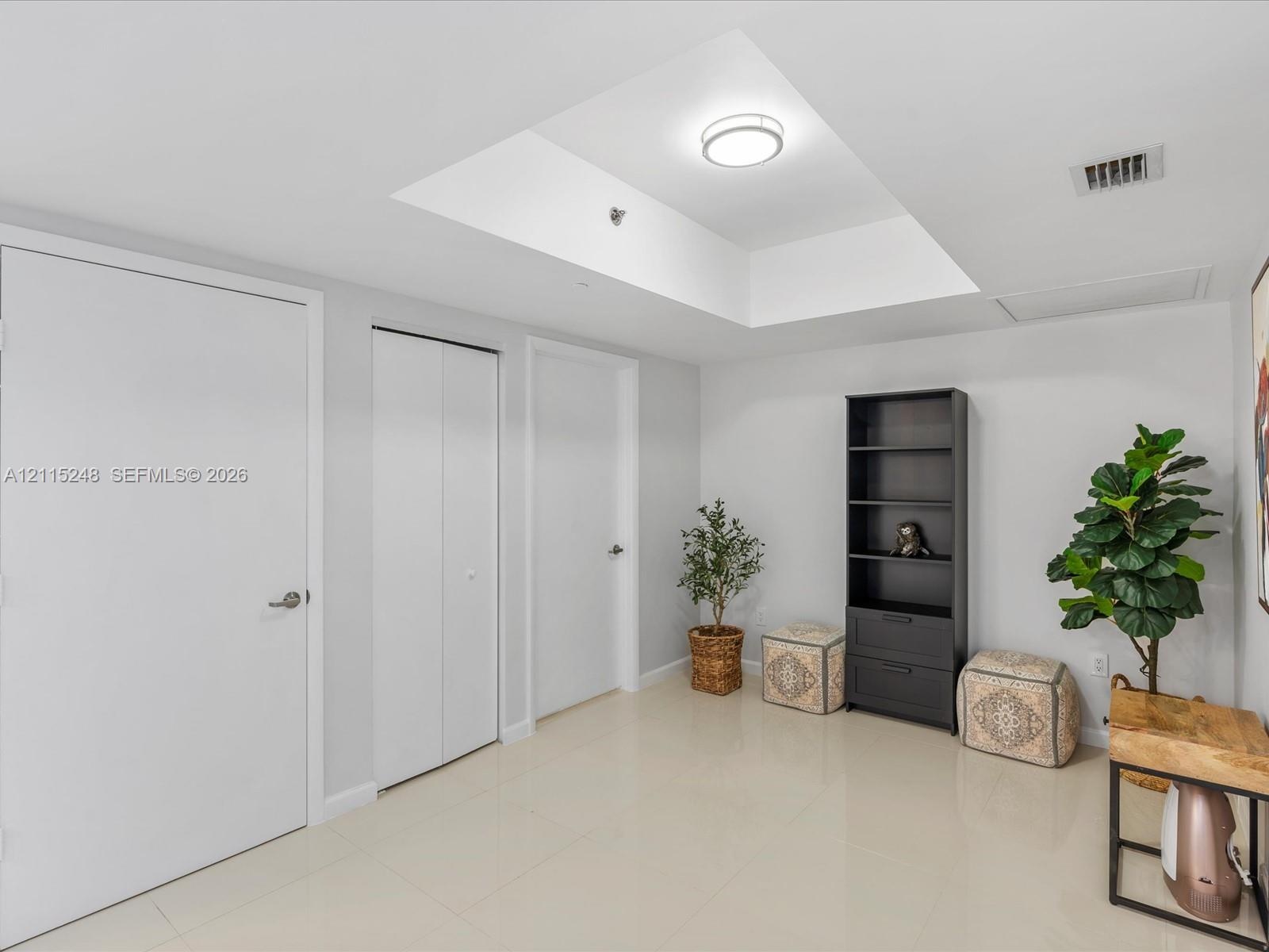Interior space featuring a recessed tray ceiling, neutral tile flooring, and multiple closet enclosures with flush-panel doors