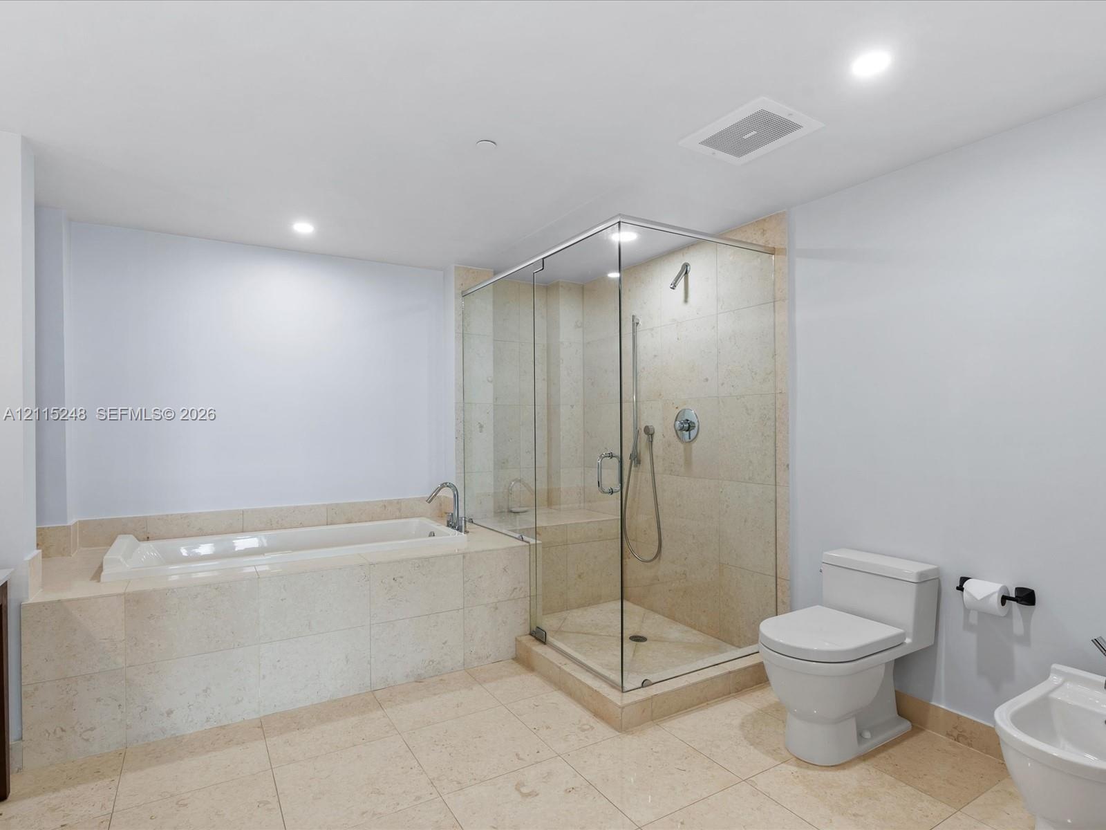 Bathroom featuring stone-tile flooring and surround, a deep soaking tub, and a frameless glass-enclosed shower with a built-in bench