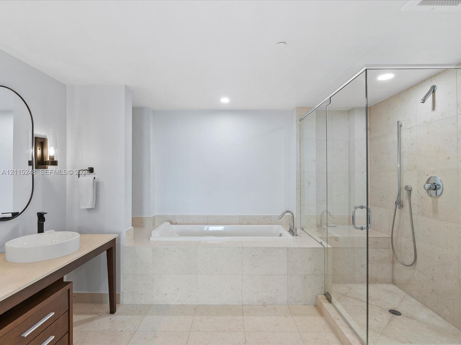 Bathroom featuring a stone-tile surround soaking tub, a frameless glass-enclosed shower with handheld fixture, stone-tile flooring, and a floating van