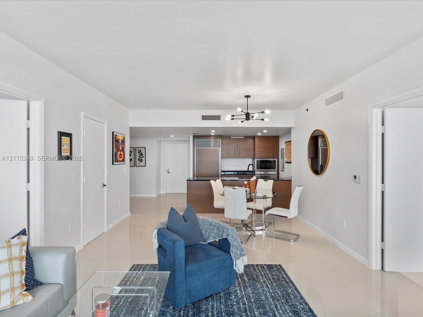 Open floor plan featuring light-toned tile flooring, recessed ceiling lighting, contemporary multi-arm chandelier, and kitchen cabinetry with integrat