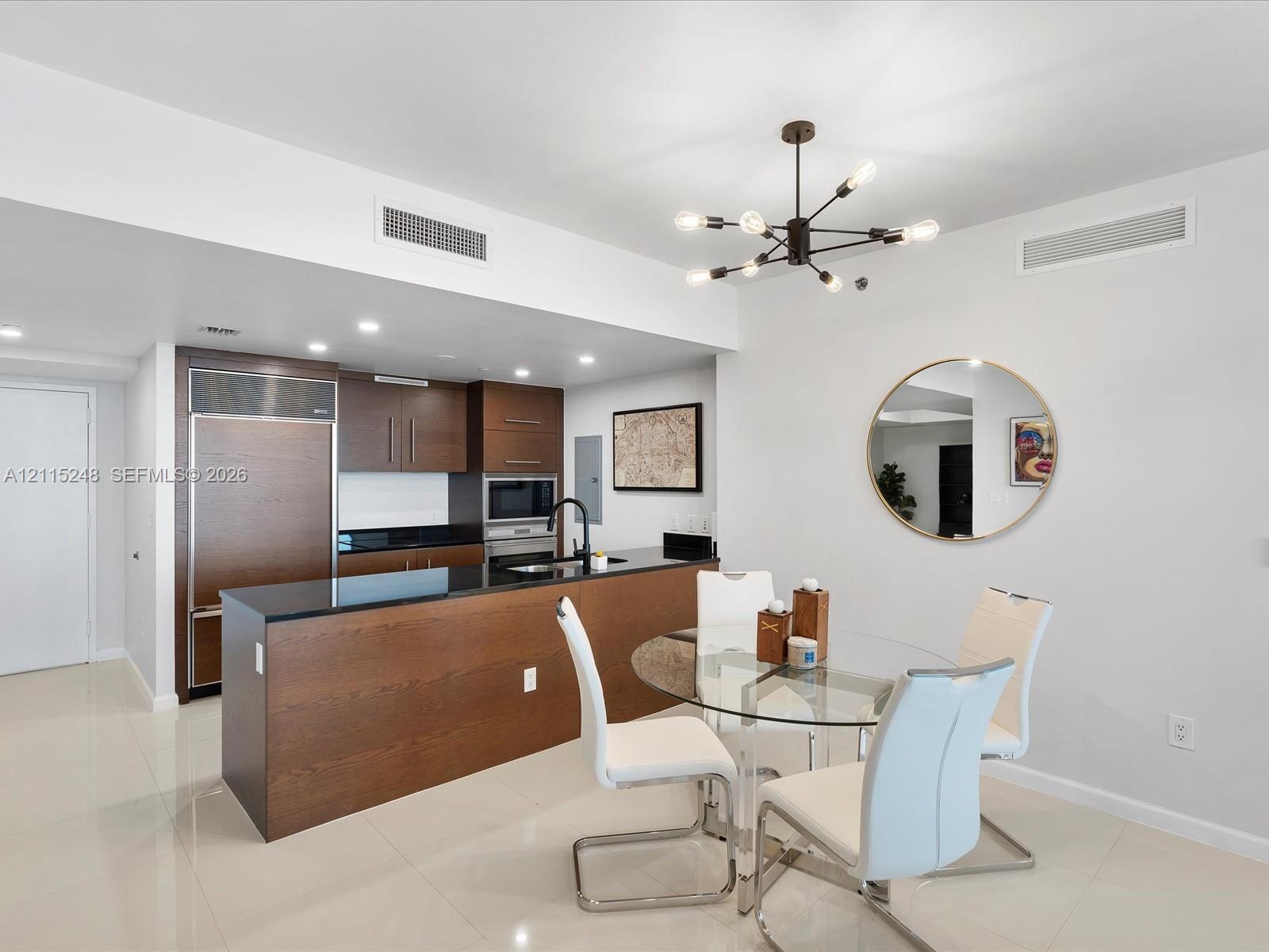 Kitchen featuring wood-finish cabinetry, black stone countertops, built-in refrigerator, matte black faucet, and modern multi-arm chandelier