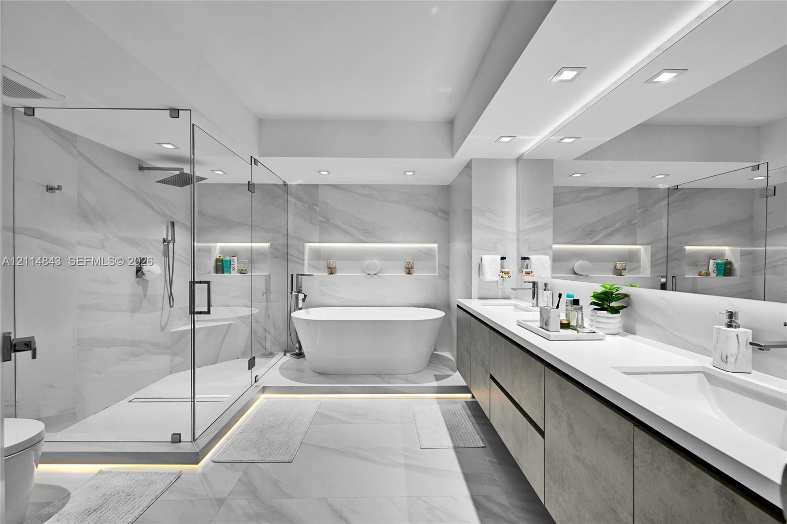 Bathroom featuring a glass-enclosed walk-in shower, freestanding soaking tub, dual-sink vanity with stone countertop, recessed wall shelving, and larg