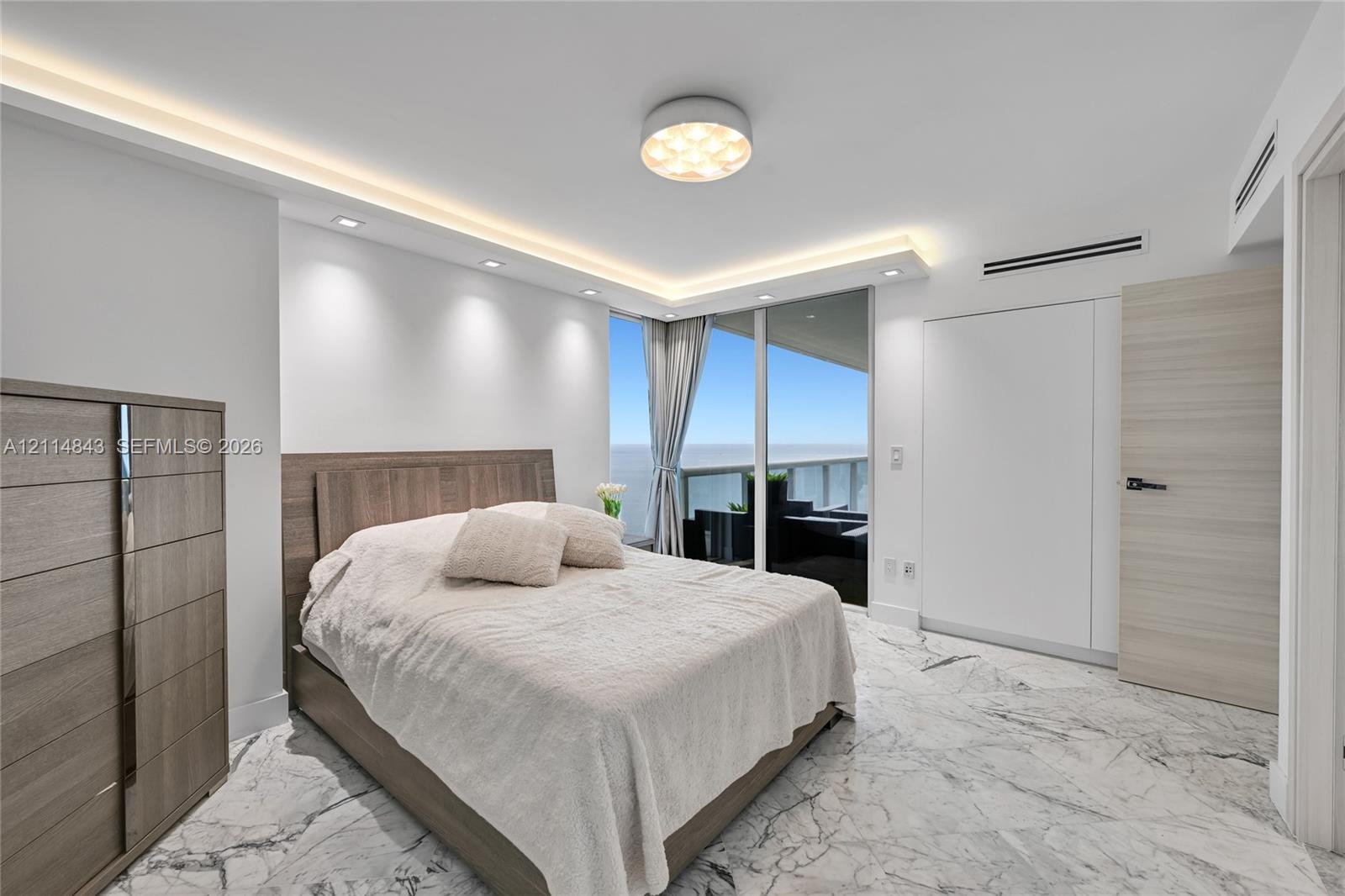 Floor-to-ceiling sliding glass doors, stone flooring with veining, recessed lighting, cove lighting, and a neutral wood-finish interior door