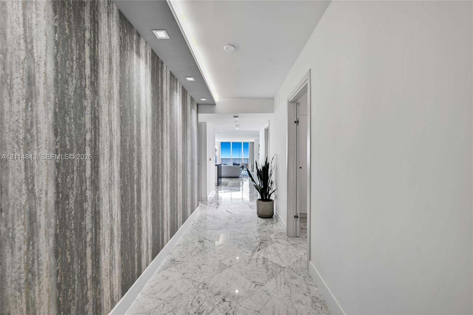 Hallway featuring stone-finish flooring, a decorative textured accent wall, and recessed architectural ceiling lighting