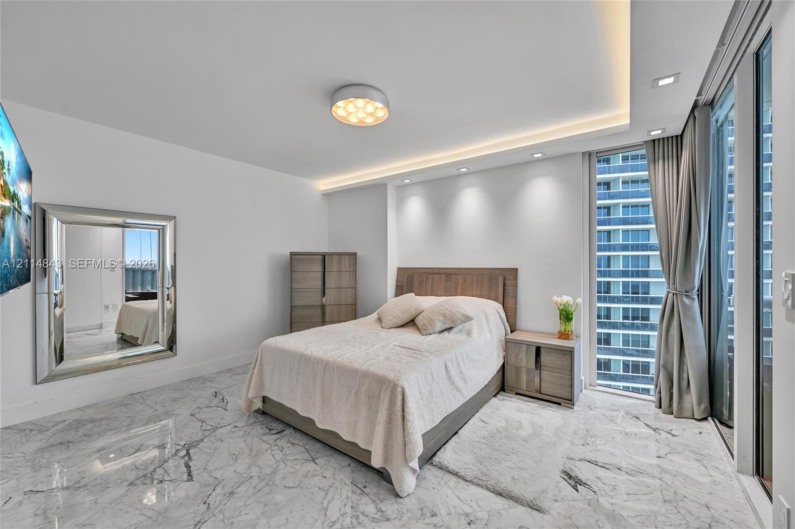 Large-format stone flooring, recessed ceiling lighting with cove accent, floor-to-ceiling glass paneling, and a contemporary flush-mount light fixture