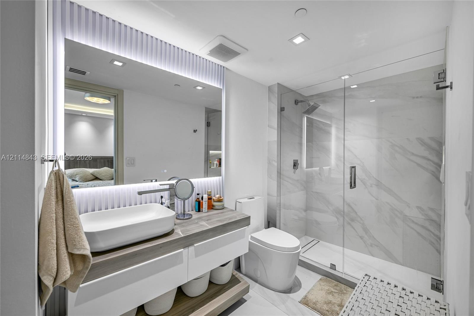 Floating vanity with a rectangular vessel sink and wood-finish countertop, full-height backlit mirror, walk-in glass shower enclosure with stone-finis