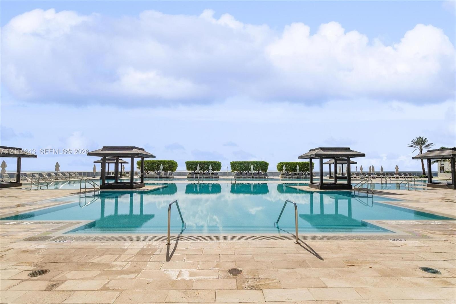 Expansive swimming pool featuring built-in cabanas, stone-paver decking, and stainless steel handrails