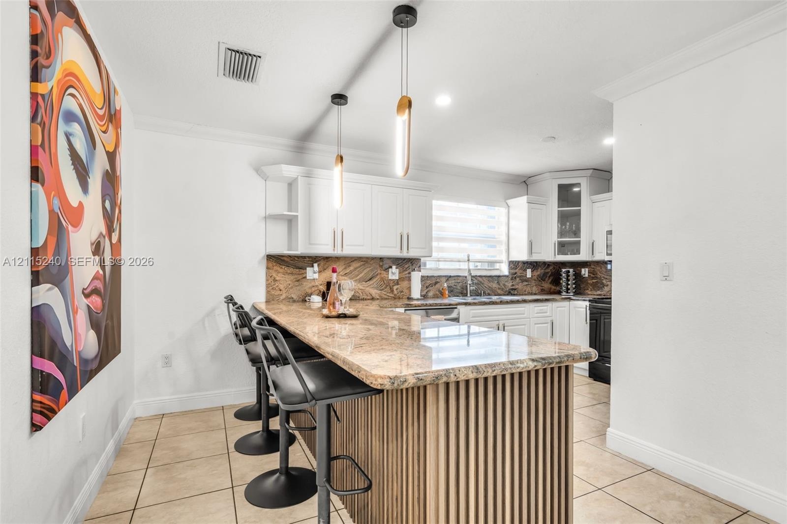 Kitchen featuring a stone-surface breakfast bar, custom-fluted wood detailing, white cabinetry, a stone backsplash, and modern pendant lighting
