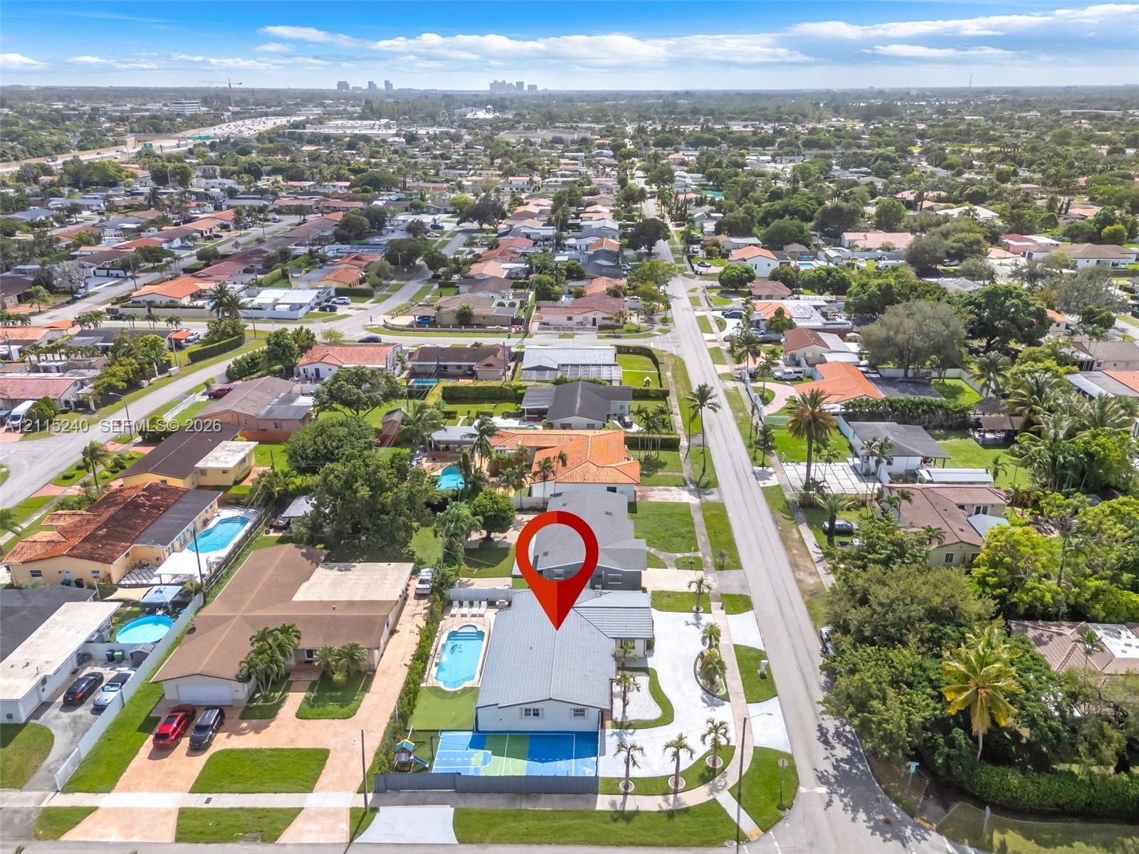 Aerial perspective of a property featuring an in-ground swimming pool, a private sports court, a paved driveway, and mature perimeter landscaping