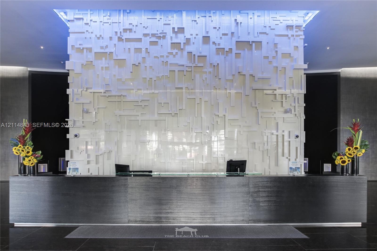 Lobby reception area featuring a high-contrast design, large-scale black service desk, three-dimensional textured accent wall, recessed cove lighting,