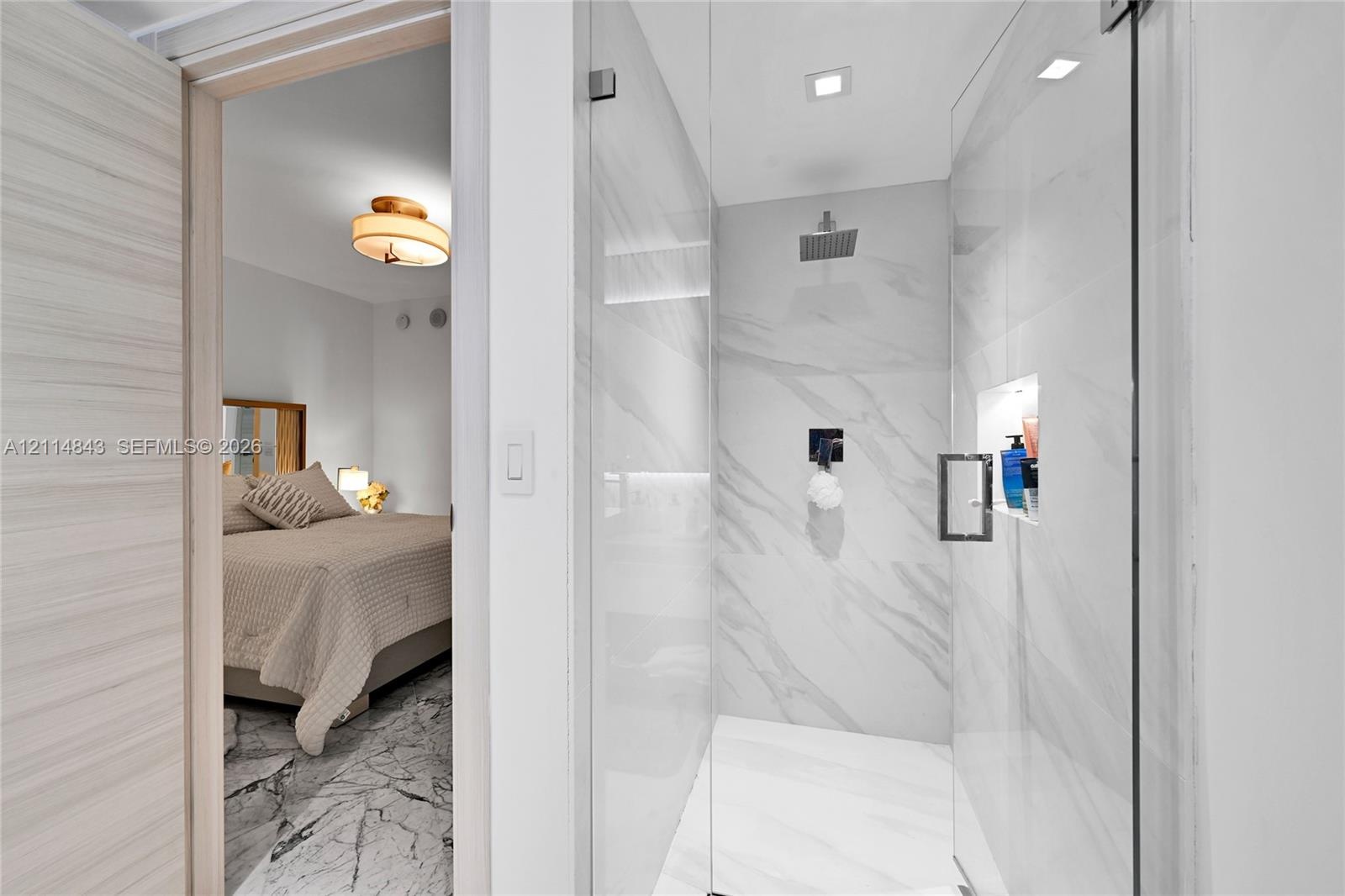 Walk-in shower featuring large-format stone-look tile, glass enclosure, recessed storage niche, and ceiling-mounted rain shower head