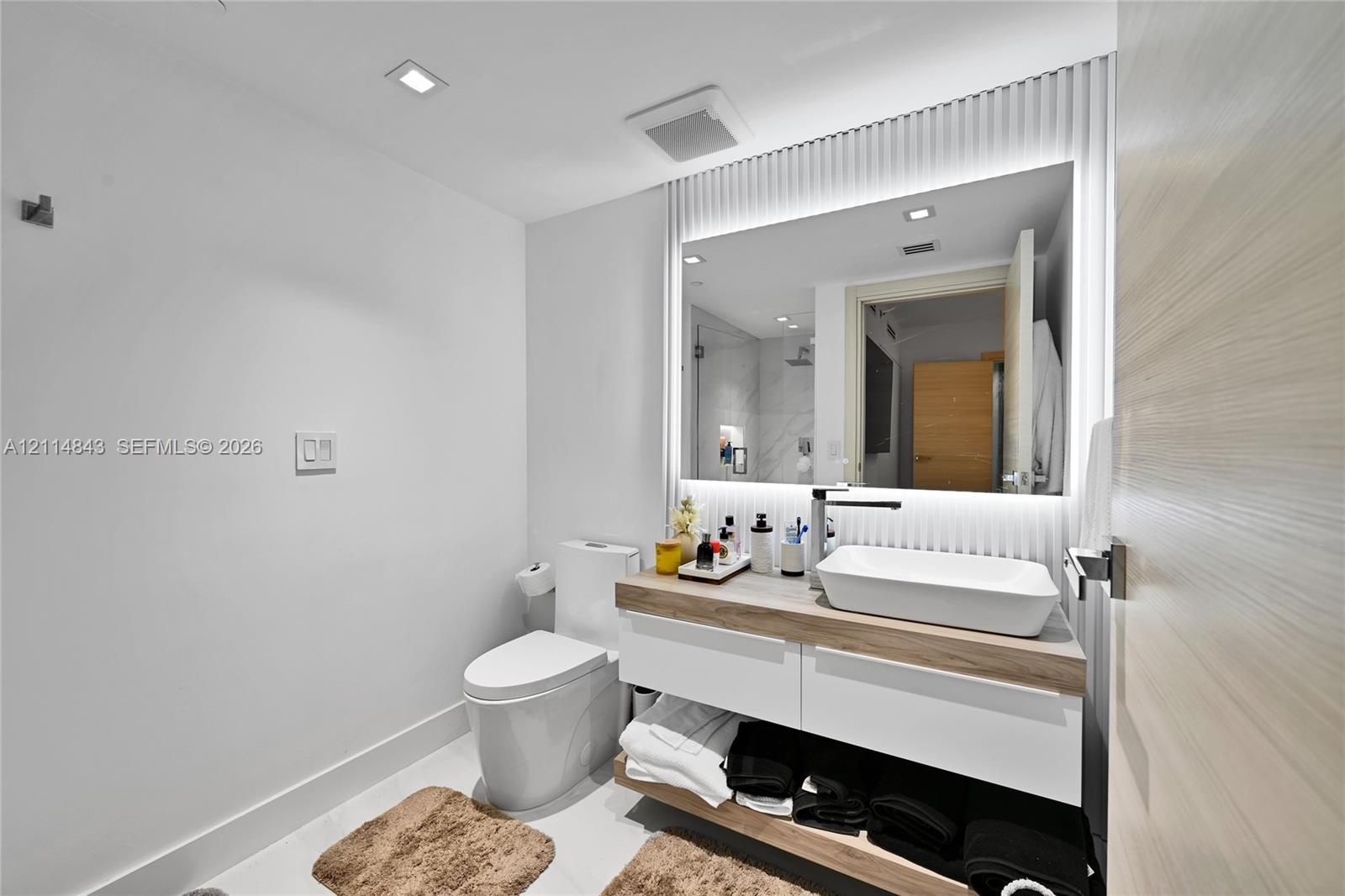 Floating vanity featuring a wood-finish countertop, white rectangular vessel sink, integrated LED mirror lighting, and vertical-slat wall paneling