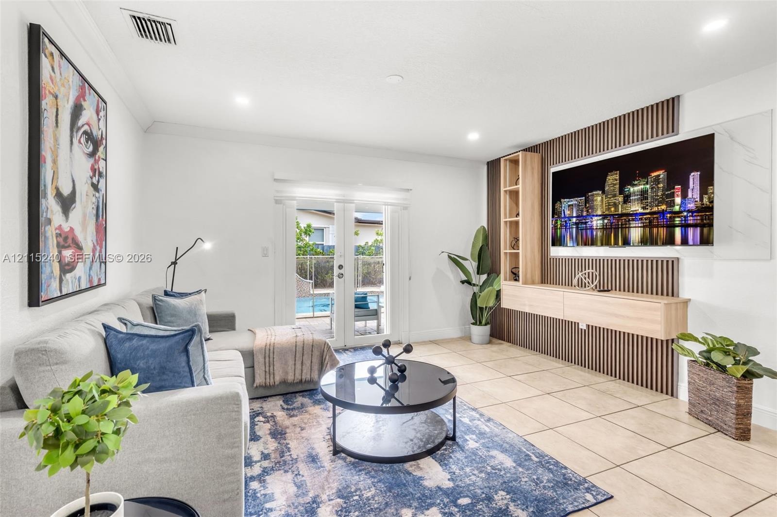 Living area featuring a custom media wall with vertical wood slats, built-in light wood cabinetry, recessed lighting, tile flooring, and glass-paned d