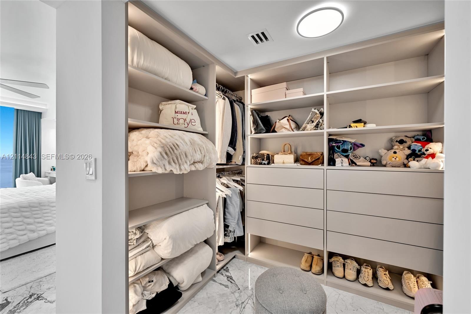 Custom walk-in closet featuring floor-to-ceiling built-in cabinetry, integrated LED shelf lighting, multiple soft-close drawers, and marble-finish flo