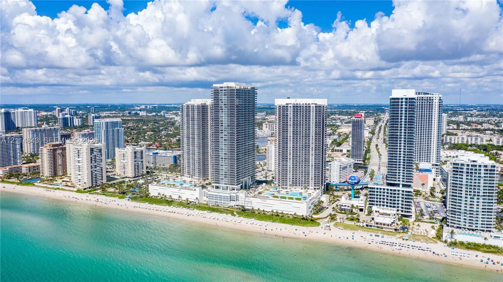 Aerial perspective of a coastal high-rise development featuring direct oceanfront access, exterior balconies, swimming pool decks, and proximity to th