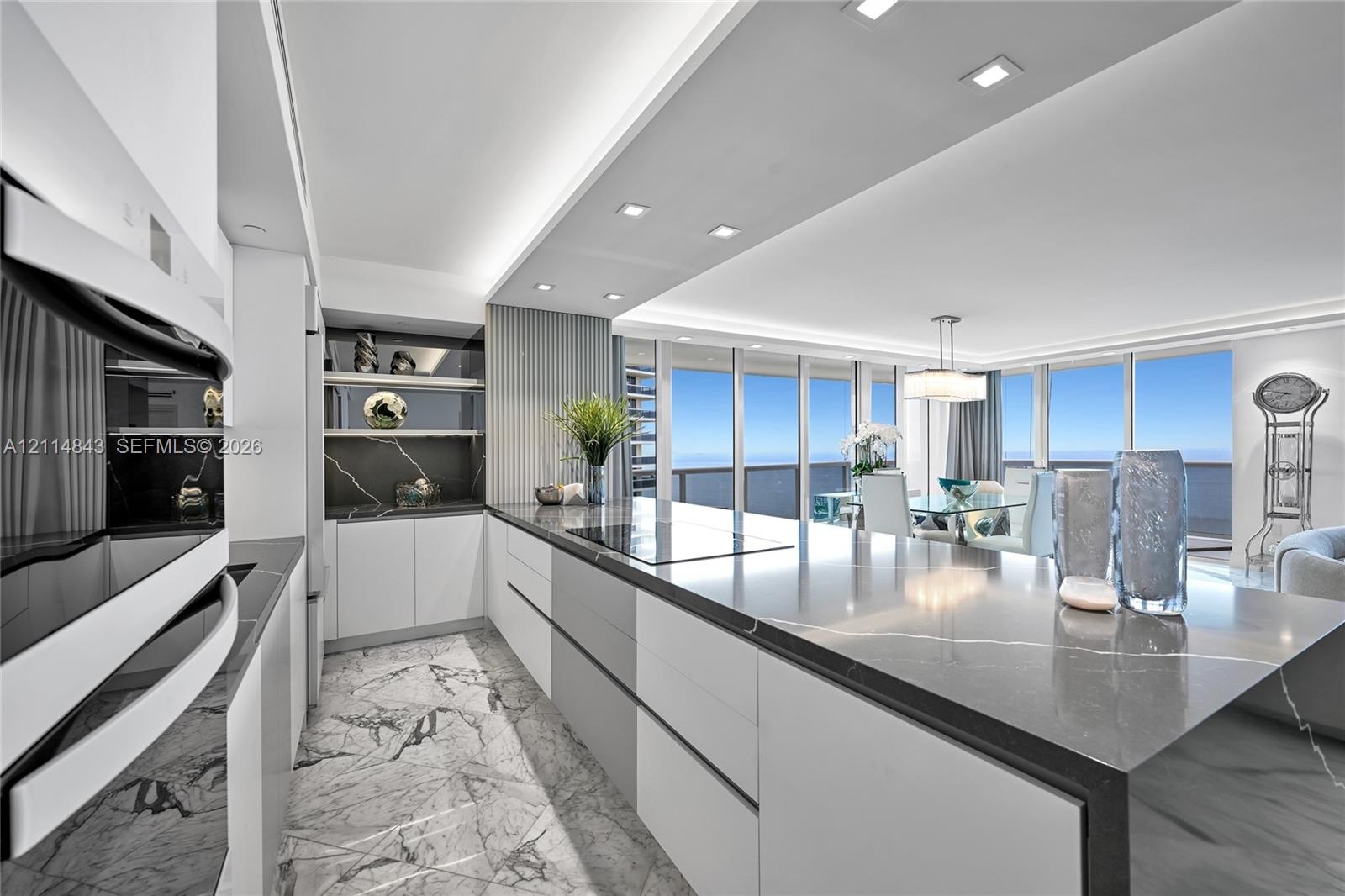Contemporary kitchen featuring custom flat-panel cabinetry, a large waterfall-edge island with solid surface countertop, built-in appliances, recessed