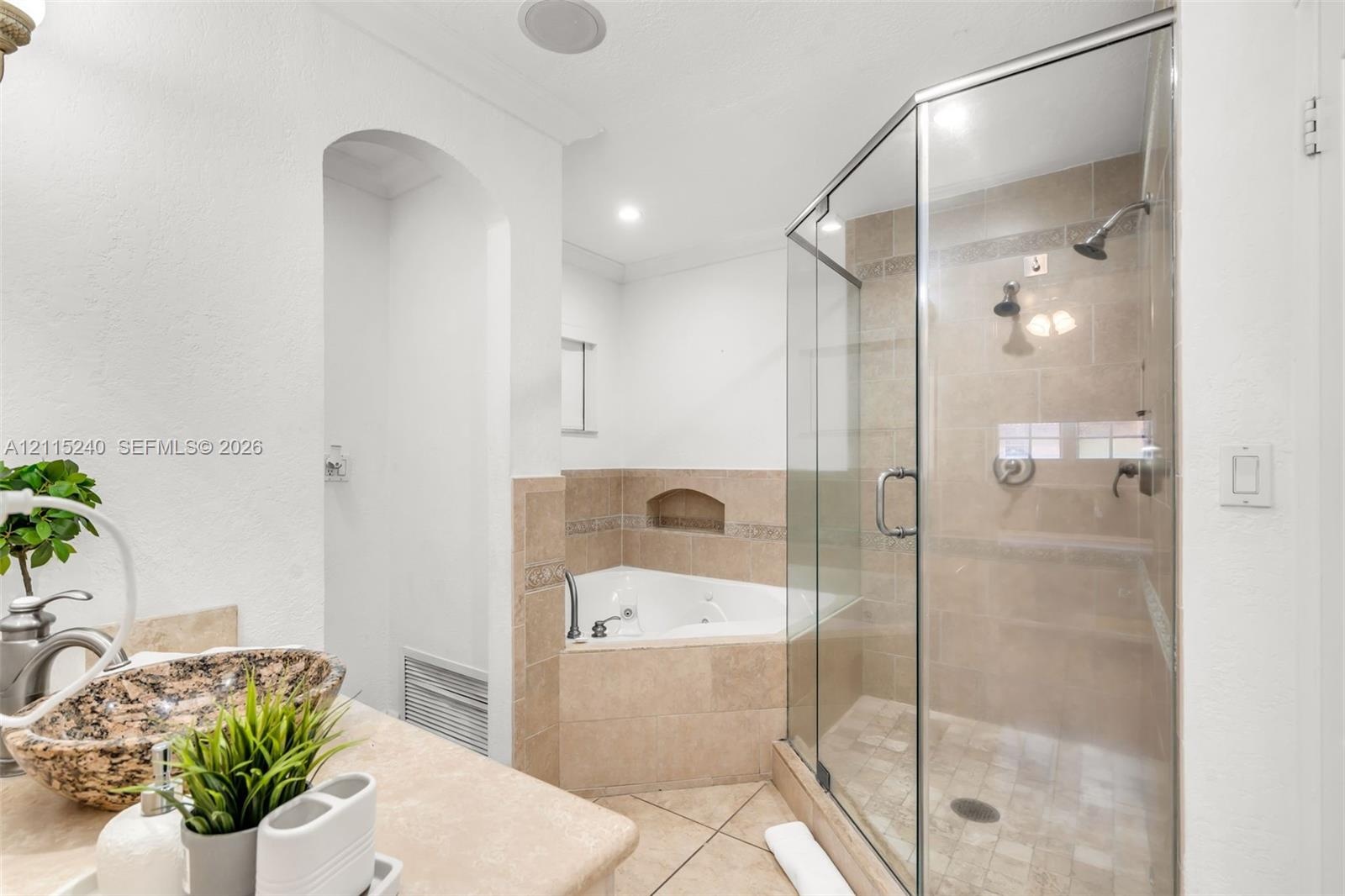Corner soaking tub with tile surround, glass-enclosed walk-in shower with stone-style tile, and natural stone countertop with vessel sink