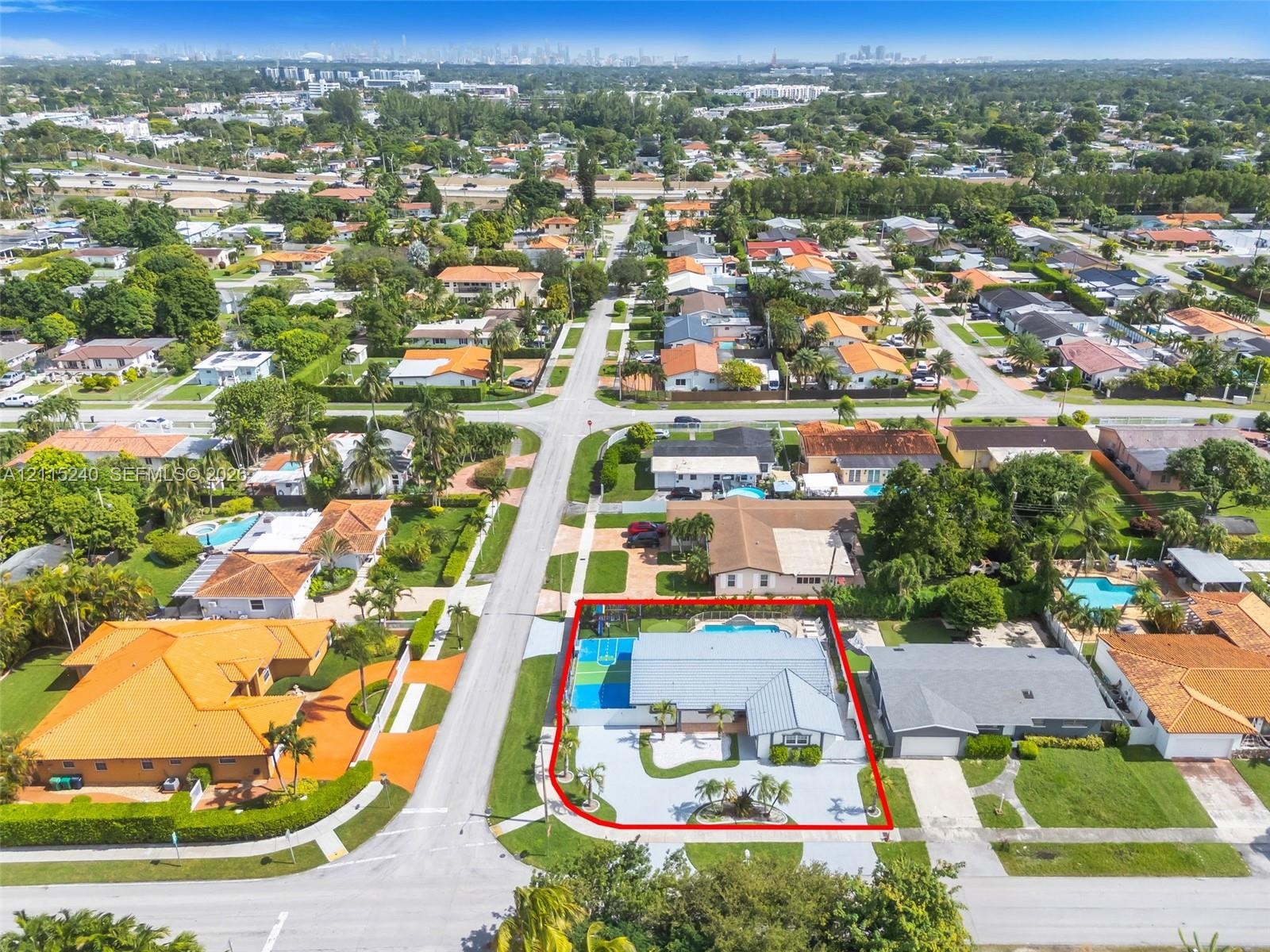 Aerial perspective of a corner lot property featuring a multi-pitched roof, an expansive paved driveway, a gated swimming pool, and a dedicated athlet