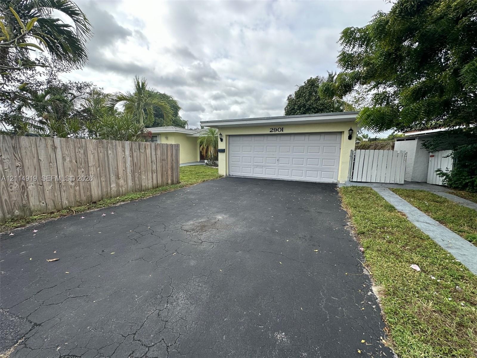 Single-story exterior featuring a two-car garage, asphalt driveway, and wood-panel perimeter fencing