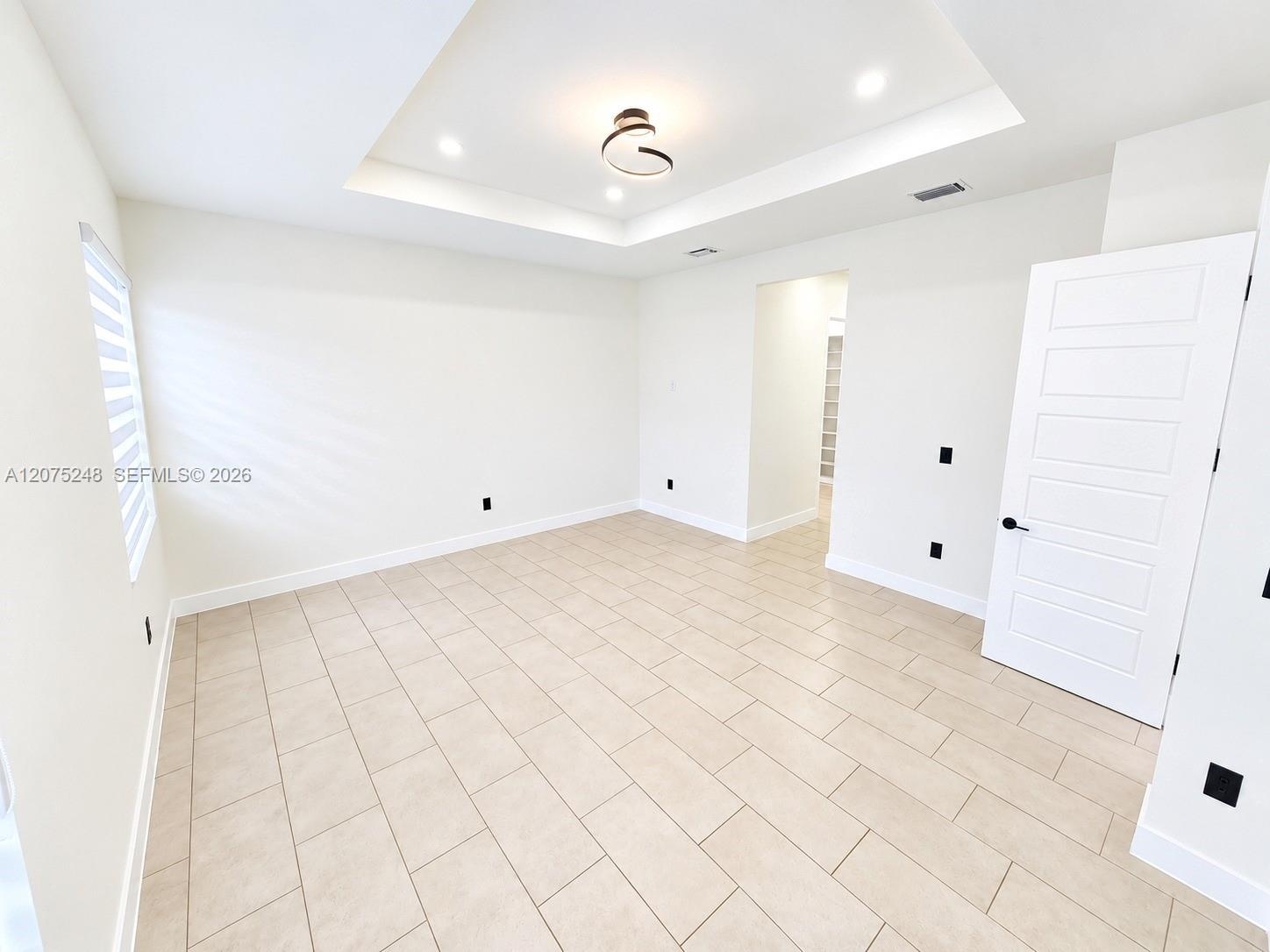 Tray ceiling featuring recessed lighting and a central contemporary light fixture, complemented by tile flooring and a five-panel interior door