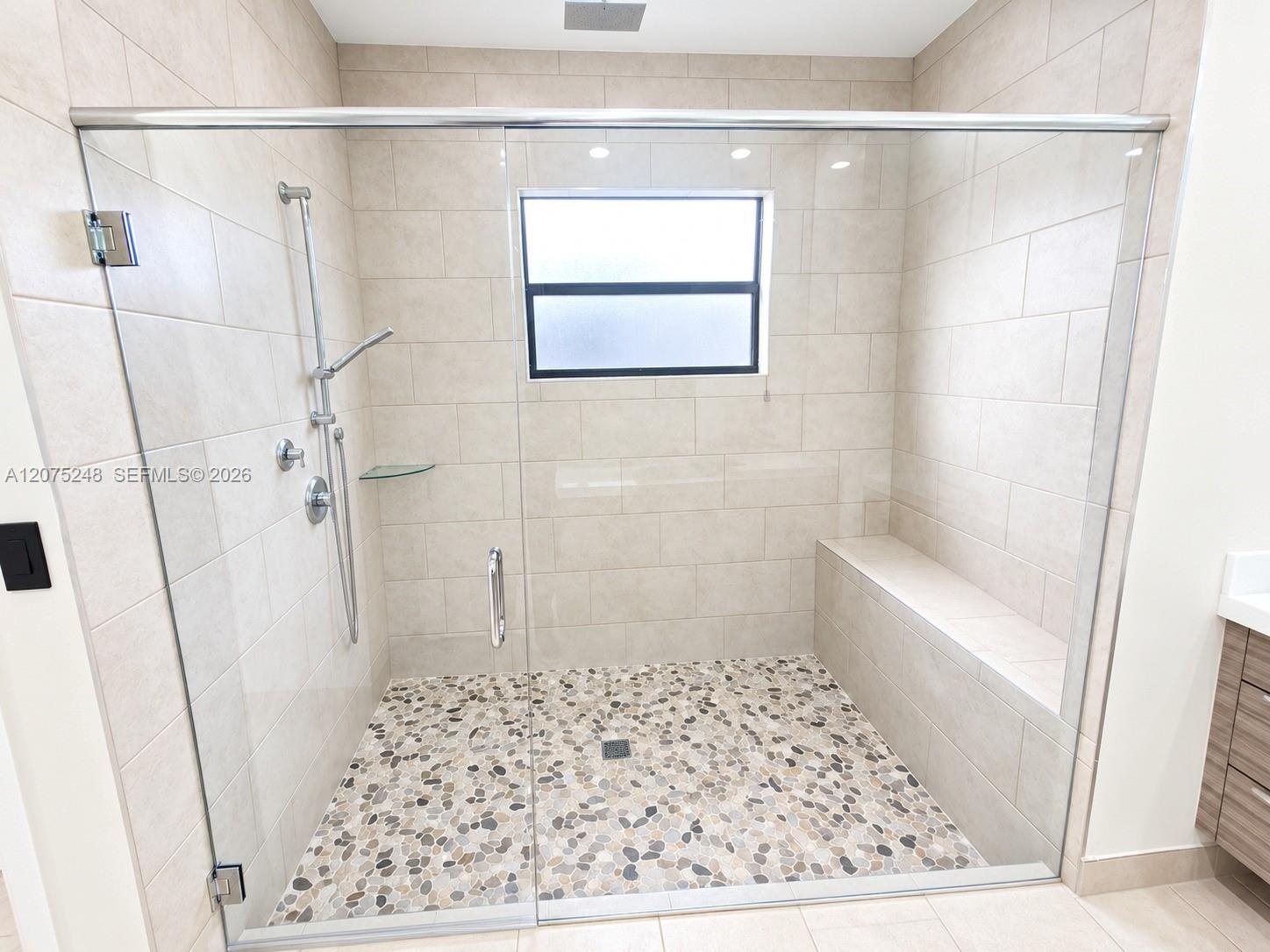 Walk-in shower MASTERS featuring a glass enclosure, pebble-stone flooring, built-in bench, wall-mounted shower head with hand-held attachment, and neu