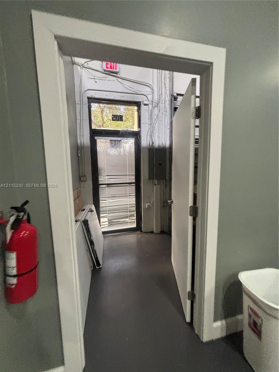 Entryway featuring a solid door, painted gray interior walls, exposed electrical conduit, and a glass-paneled exterior door with integrated horizontal