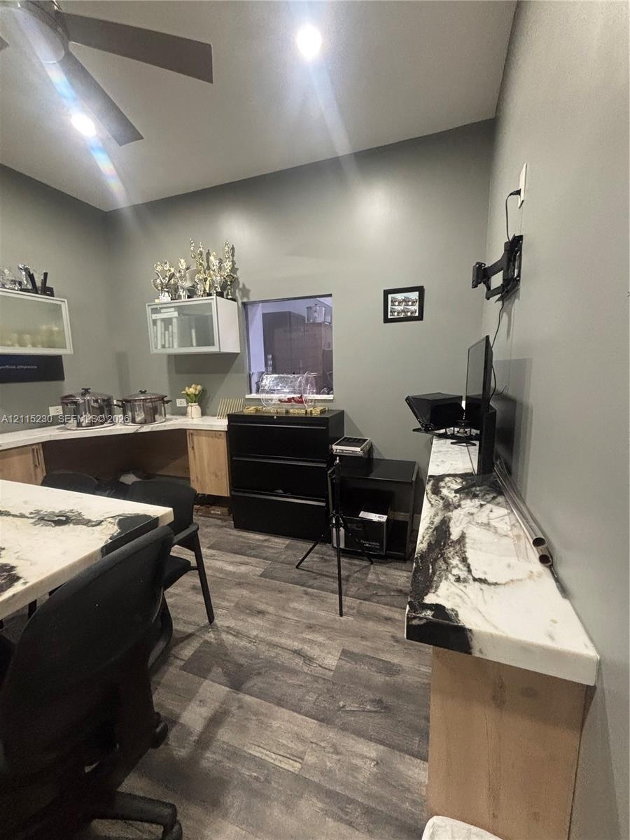 Room featuring wood-finish flooring, built-in cabinetry with light-toned wood base, stone countertops with distinctive veining, and a wall-mounted cei