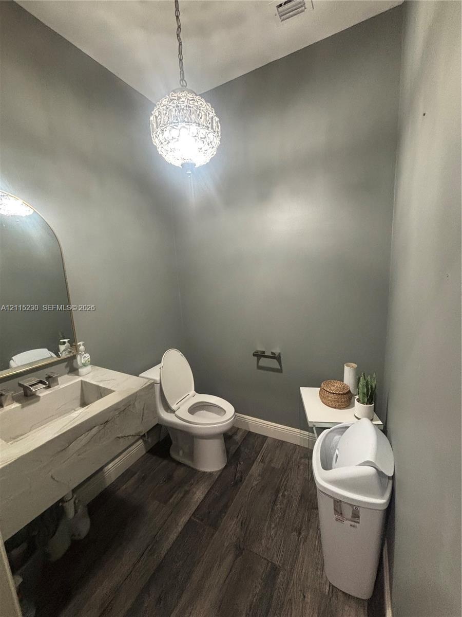 Floating vanity with integrated basin, stone-finish countertop, arched wall mirror, dark wood-finish flooring, and decorative crystal pendant lighting
