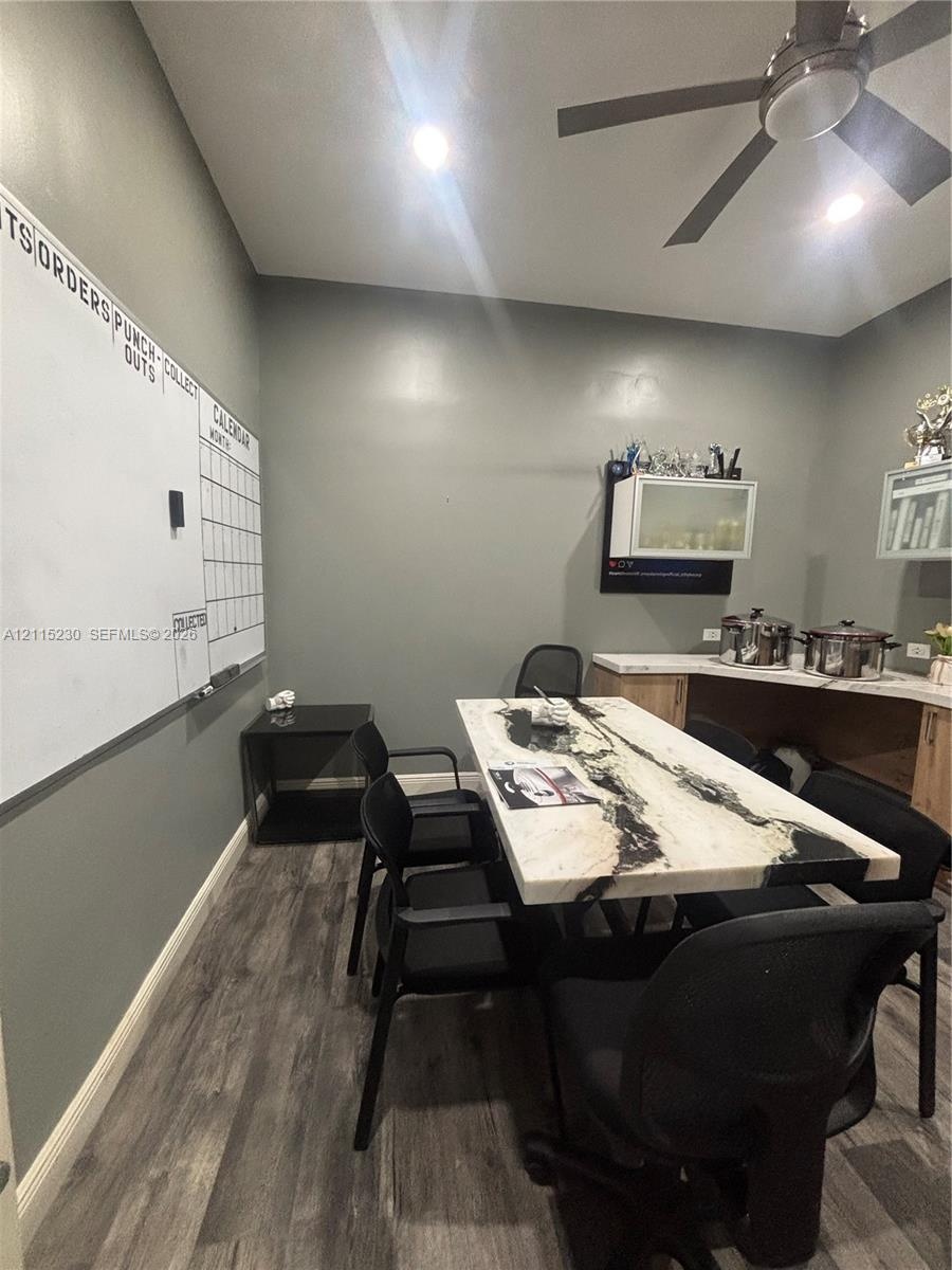 Room featuring wood-finish flooring, built-in cabinetry with stone-finish countertops, wall-mounted glass-front cabinetry, and a ceiling-mounted fan