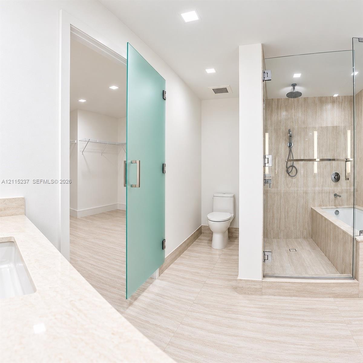 Bathroom featuring stone-finish floor and wall tiles, glass-enclosed shower with integrated tub, frosted glass door, and neutral-toned countertop with